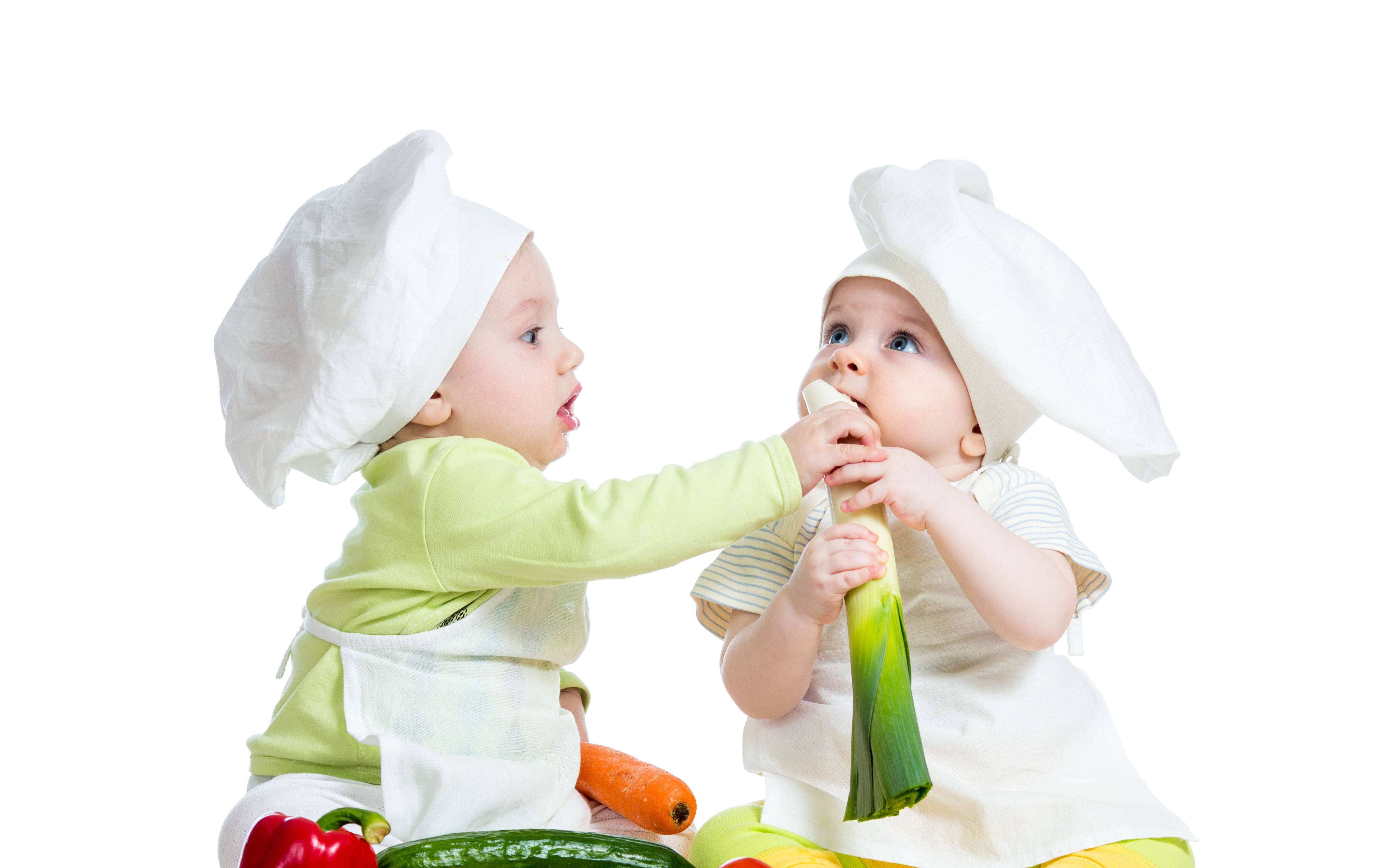 2 babyer der sidder med forskellige grøntsager og giver hinanden mad